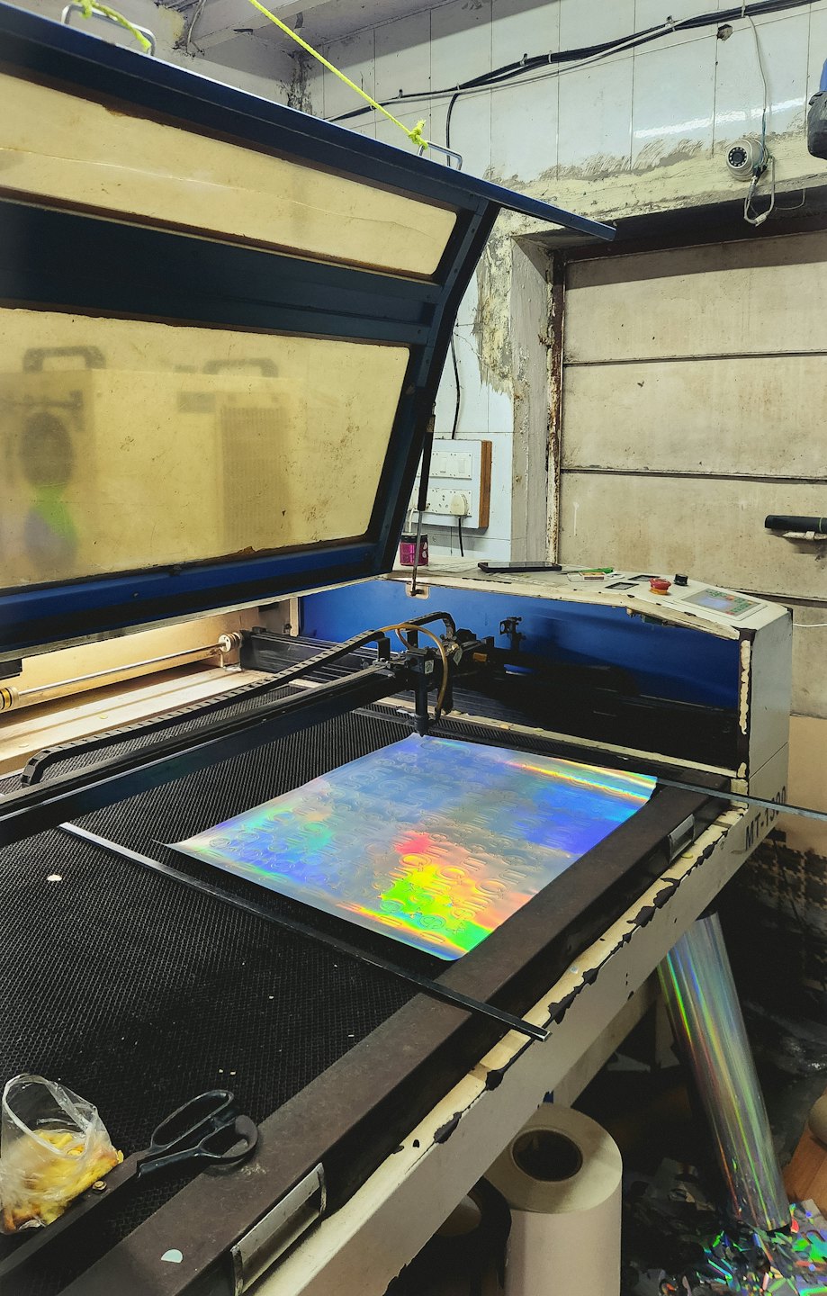Laser cutter processing iridescent holographic material in a workshop.