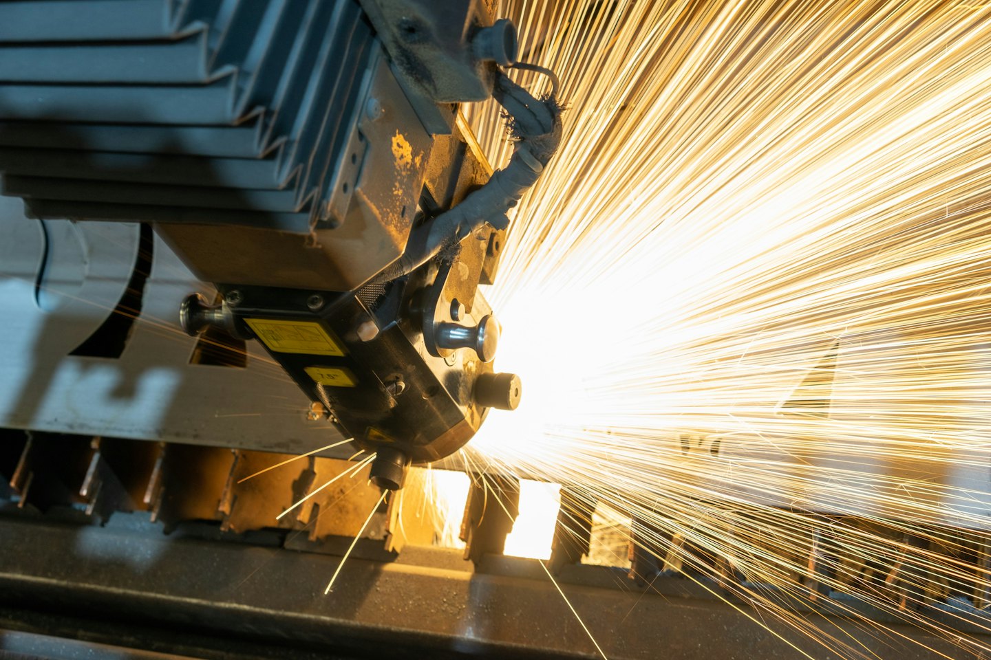 Laser cutting machine sparks fly as it cuts dark metal.